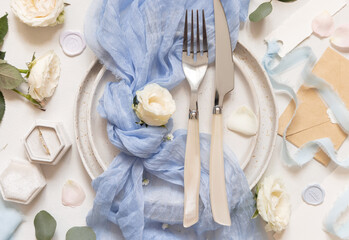 Wedding table place with with fork and knife, blue tulle fabric and cream flowers top view