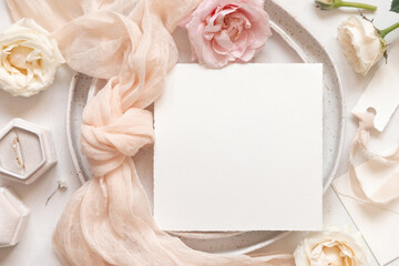 Square card near cream roses and petals, ring and silk ribbons top view, wedding mockup