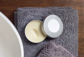 Jar of body butter with round label on grey towel near basin on wood in bath, mockup