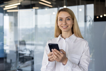 Smiling businesswoman using smartphone in modern office with glass walls