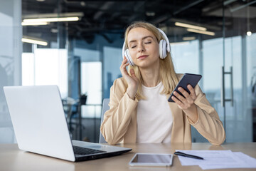 Businesswoman relaxing at work with headphones and smartphone in a modern office