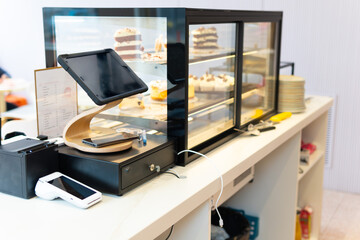 Interior of a pastry cafeteria counter with tablet, wireless card reader and cash register.