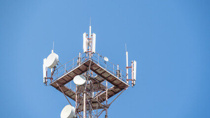 Naklejka premium A closeup and detailed view of various GPS, cellphone, 3G, 4G and 5G equipped telecommunication tower as seen on cloudy blue sky with copy space. Antennae background of cloudy sky and space for text