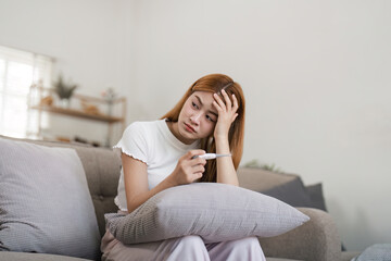 Sick woman checking temperature with thermometer while resting on couch at home. Concept of...