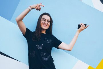 Happy young woman in spectacles for vision correction feeling excited near colorful wall and...