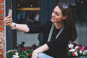 Positive female student spending time on urban setting and taking selfie pictures for own internet...