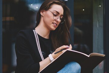 Attractive clever hipster girl studying in university campus holding textbook for education and...