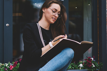 Attractive clever hipster girl studying in university campus holding textbook for education and...