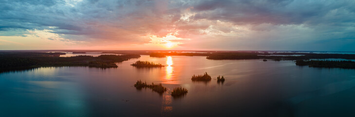 Aerial view of a large lake with small islands at sunset. The setting sun and colorful clouds are reflecting in the calm water.
