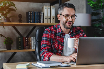 Mid adult man freelancer manager worker using laptop typing looking at screen working remote on...