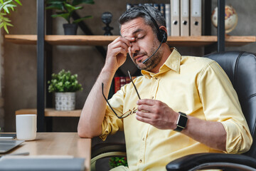 Business operator exhausted man wearing customer service headset from call center suffering from...