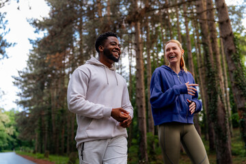 Two friends running through a scenic forest path, sharing joy and fitness. Wearing hoodies and...