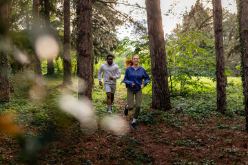 Fototapeta premium Two friends jogging through a dense forest area, sharing a moment of fitness and fun. They are dressed in sportswear, highlighting their active lifestyle.