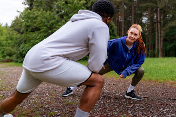 A couple stretching and preparing for a jog in the forest. They are smiling and dressed in...