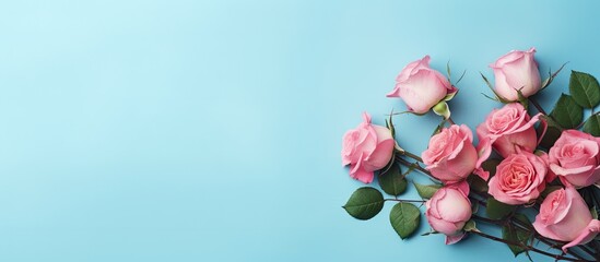 A floral arrangement featuring pink roses adorns a pastel blue backdrop in a flat lay view There is ample copy space within the image