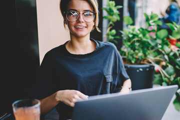 Portrait of cheerful female student looking in camera during searching new interesting websites via...