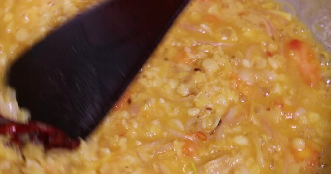 Adding boiling dal lentil into bagar tadka with deep fry tomato onion garlic cumin red dry chilli spice stair cooking dal ghotni whisk 