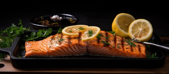 A grilled salmon is presented on a black pan with a lemon slice and spatula resting on a wooden surface This captivating image can be used as a background wallpaper or for copy space