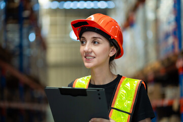 A woman wearing a safety vest and a hard hat is holding a clipboard. She is smiling and she is happy