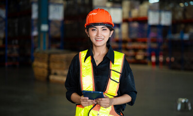 A woman wearing a safety vest and a hard hat is holding a tablet. She is smiling and she is happy