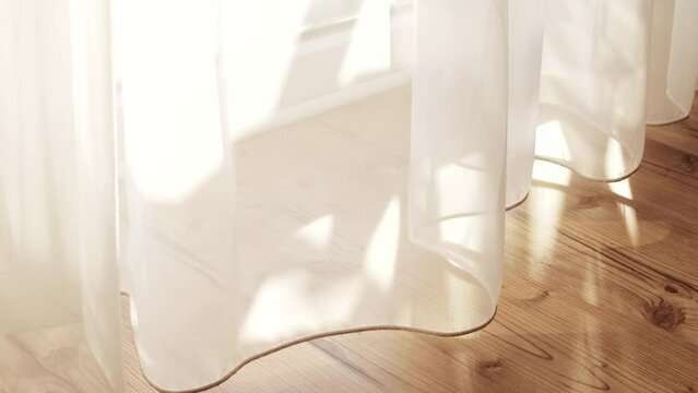 Transparent white curtain tulle moves from the wind from an open window. Sunny day, the sun's rays sunlight penetrate the room.	