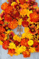 orange-red colorful flowers and wooden christian cross on table. top view. Symbol of the death and...