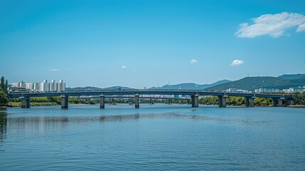 Obraz premium the picturesque cityscape and bridge on a sunlit day, where tranquil waters reflect the clear blue sky dotted with wispy clouds.