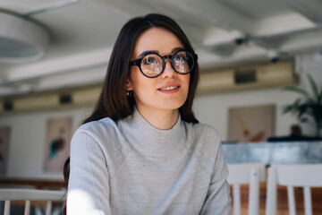 Female student learning at cafeteria while looking away and smiling, happy blogger enjoying time at...