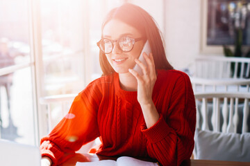 Positive hipster girl working online as successful freelancer while calling to customer service for...