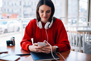 Positive female student reading email and choosing playlist via smartphone connected to wifi, happy...