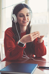 Smiling teenage meloman enjoying favourite music via earphones while chatting with friends via...