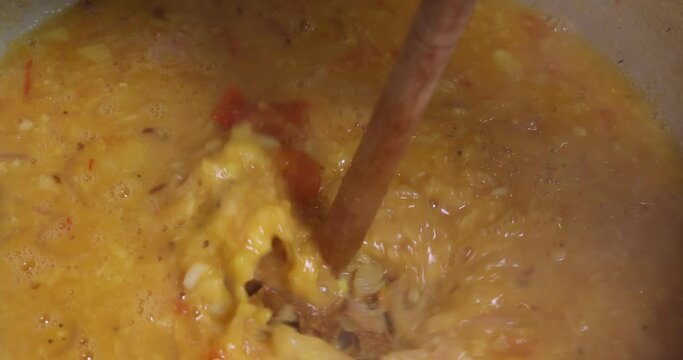 Adding boiling dal lentil into bagar tadka with deep fry tomato onion garlic cumin red dry chilli spice stair cooking dal ghotni whisk 