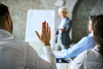 Businessman raising his hand to ask a question on a seminar in board room.