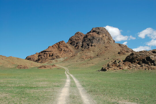 a long dirt road through an alpine meadow into the mountains; summer, Mongolia