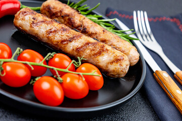 Grilled sausages with tomatoes and hot peppers on a black plate close-up