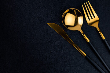 Spoon, fork and knife on black concrete background top view, space for text