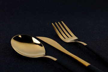 Gold plated cutlery on black concrete background close up