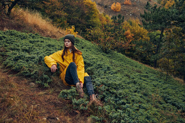 Serene woman in stylish yellow raincoat resting on autumn hilltop, contemplating nature's beauty...