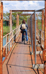 fearless young woman on a bicycle crosses a dangerous and rusty iron bridge