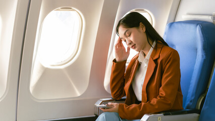 Asian woman looking at phone while sitting on airplane Technology female travelers using mobile...