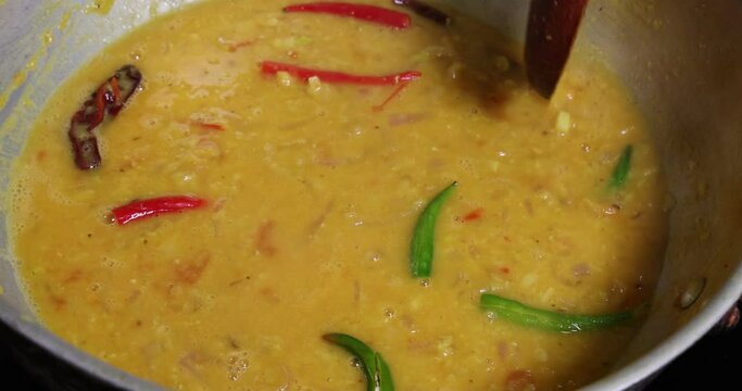 Adding boiling dal lentil into bagar tadka with deep fry tomato onion garlic cumin red dry chilli spice stair cooking dal ghotni whisk 