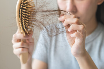 Serious asian young woman holding brush holding comb, hairbrush with fall black hair from scalp...