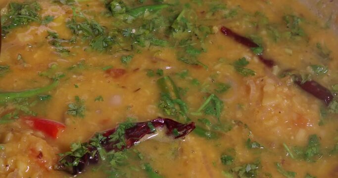 Adding boiling dal lentil into bagar tadka with deep fry tomato onion garlic cumin red dry chilli spice stair cooking dal ghotni whisk 