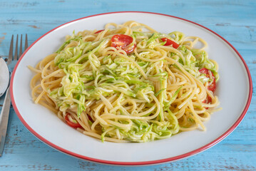 Vegetarian pasta with zucchini and cherry tomatoes on ceramic plate.