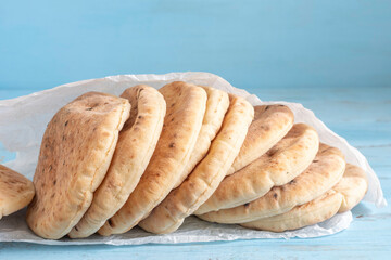Freshly baked pita bread or flatbread on textured paper over blue wooden background.
