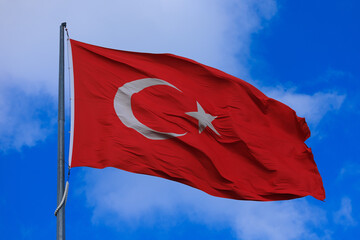 Turkish flag, on a red background white star and moon. Flag flies in the wind, public place.