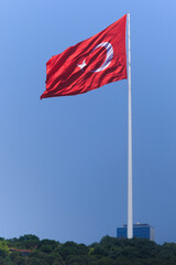 Turkish flag, on a red background white star and moon. Flag flies in the wind, public place.