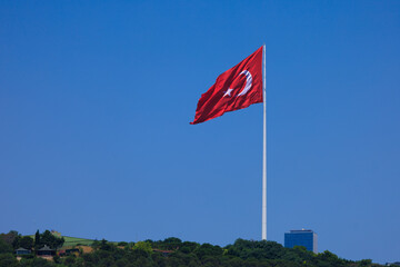 Turkish flag, on a red background white star and moon. Flag flies in the wind, public place.