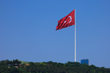 Turkish flag, on a red background white star and moon. Flag flies in the wind, public place.