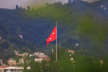 Turkish flag, on a red background white star and moon. Flag flies in the wind, public place.
